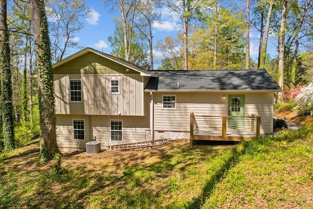 rear view of property with central AC unit, a wooden deck, a lawn, and board and batten siding