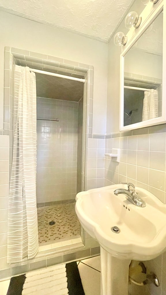 bathroom featuring tile patterned flooring, a shower with shower curtain, tile walls, and a textured ceiling