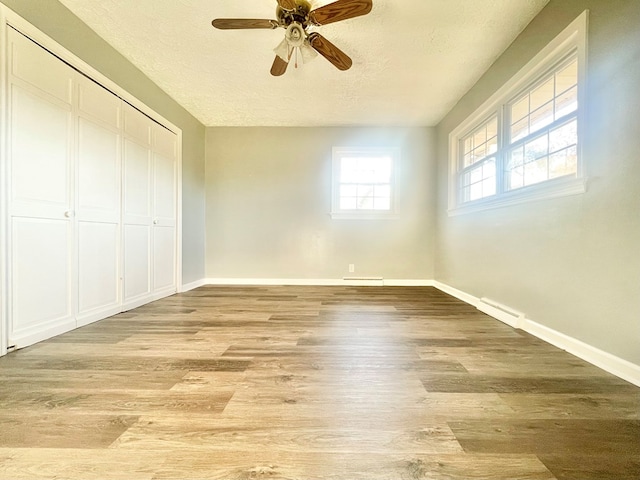 unfurnished bedroom featuring ceiling fan, a closet, light hardwood / wood-style floors, and a textured ceiling