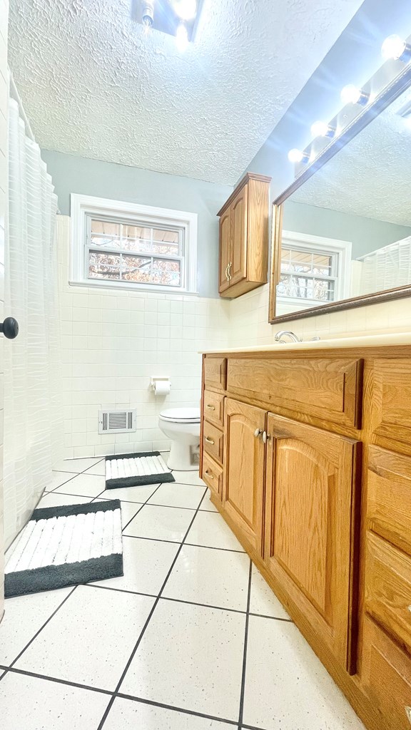 bathroom with tile walls, tile patterned floors, toilet, and a textured ceiling