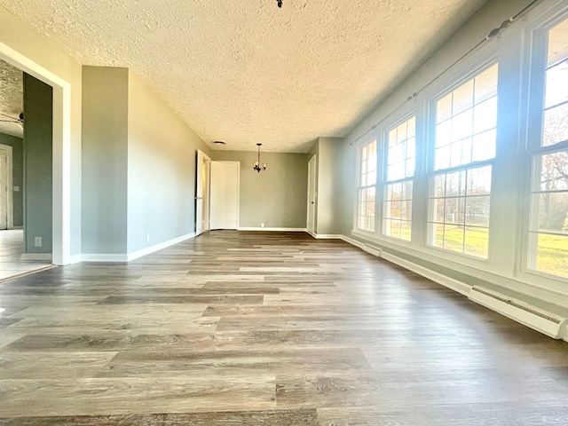 empty room with a textured ceiling, wood-type flooring, a baseboard radiator, and a healthy amount of sunlight