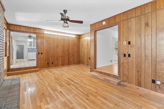 interior space with ceiling fan, light wood-type flooring, and wood walls