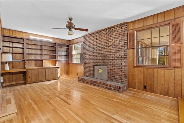 unfurnished living room featuring ceiling fan, a healthy amount of sunlight, wooden walls, and light hardwood / wood-style floors