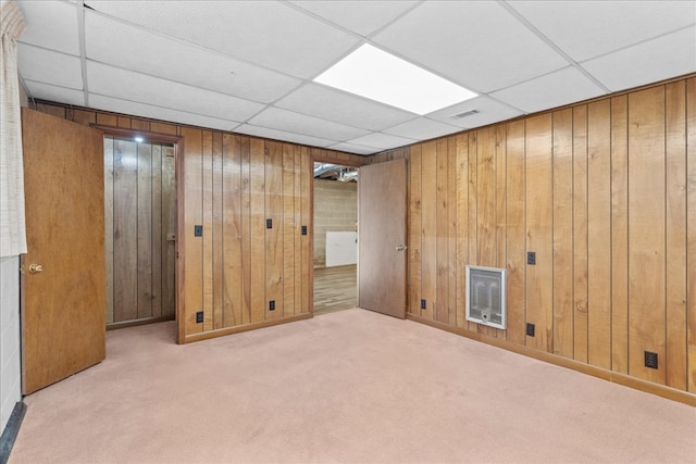 basement with heating unit, light colored carpet, a drop ceiling, and wooden walls