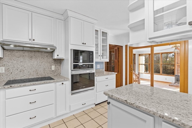 kitchen with light tile patterned flooring, black appliances, white cabinets, light stone countertops, and backsplash