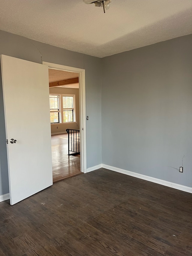 spare room with baseboards, dark wood-style floors, and a textured ceiling