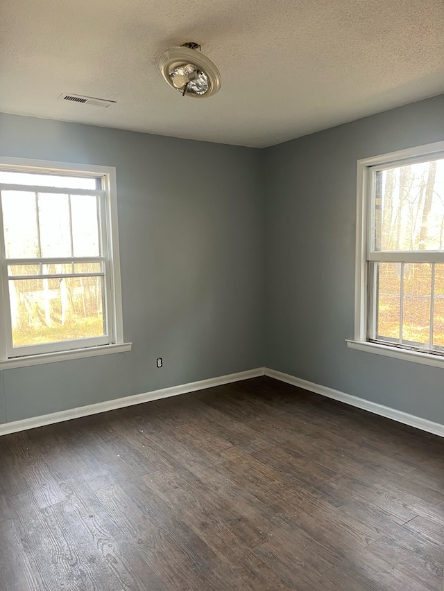 empty room with plenty of natural light, dark wood finished floors, and visible vents