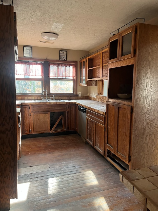 kitchen featuring stainless steel dishwasher, a sink, brown cabinetry, and hardwood / wood-style flooring