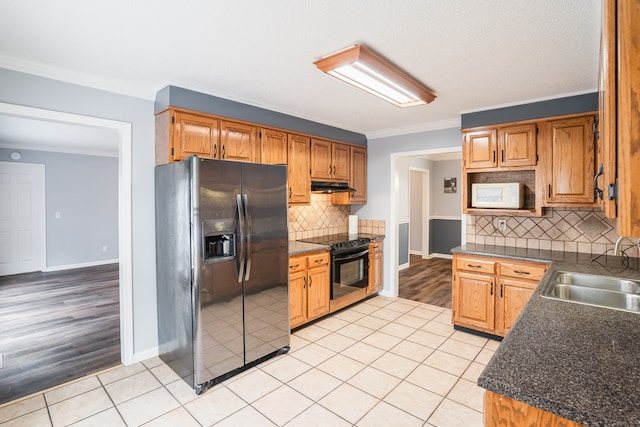 kitchen with white microwave, under cabinet range hood, light tile patterned floors, stainless steel fridge, and black electric range oven