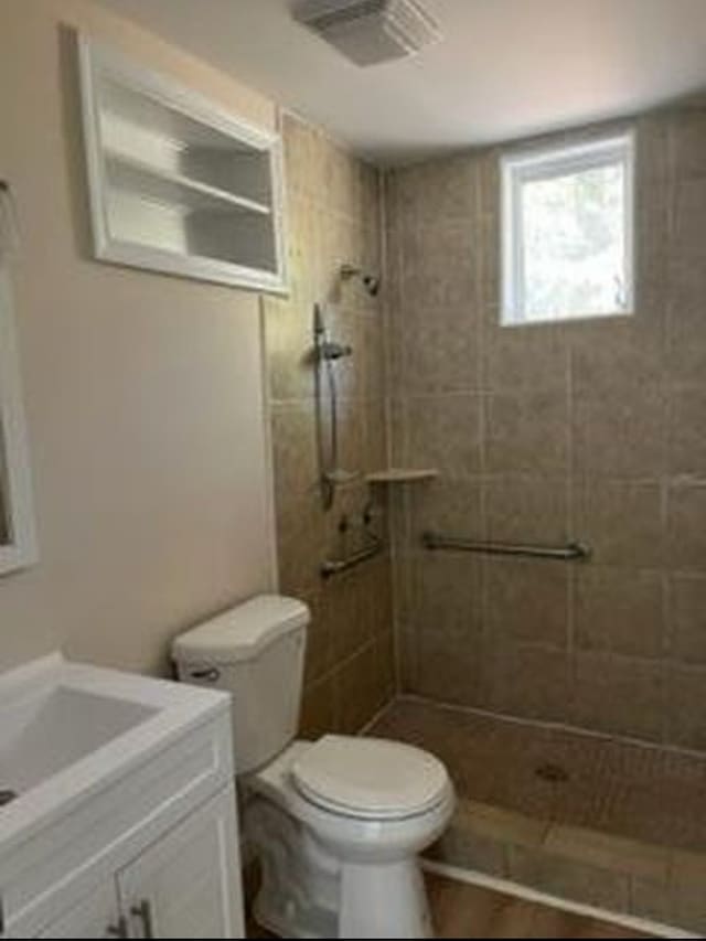 bathroom with hardwood / wood-style flooring, tiled shower, vanity, and toilet