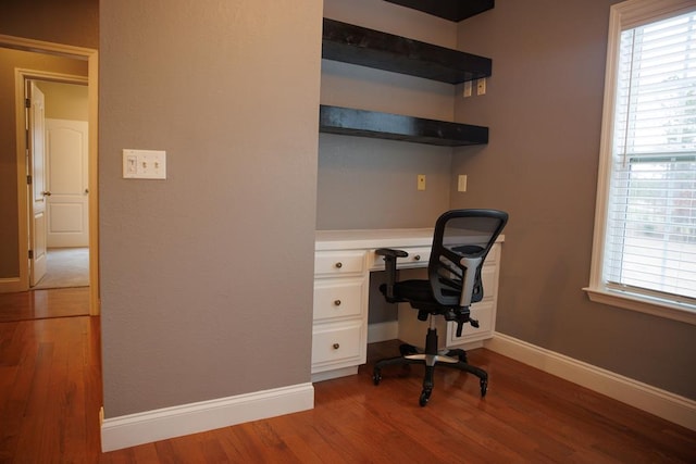 unfurnished office featuring hardwood / wood-style flooring, a healthy amount of sunlight, and built in desk