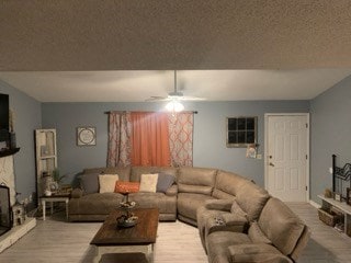 living room featuring light hardwood / wood-style flooring, ceiling fan, a textured ceiling, and a fireplace