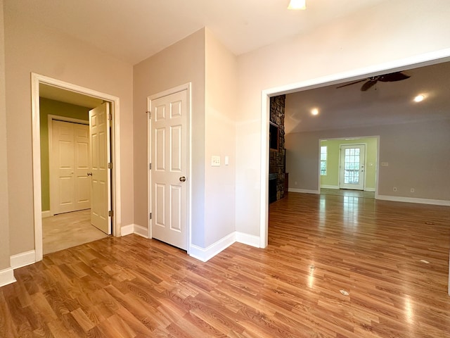 unfurnished room with ceiling fan, a fireplace, and light hardwood / wood-style flooring