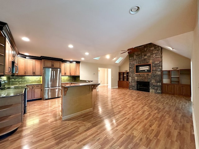 kitchen with a breakfast bar, appliances with stainless steel finishes, kitchen peninsula, vaulted ceiling with skylight, and light hardwood / wood-style floors