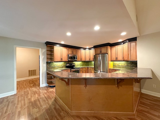 kitchen with a breakfast bar, kitchen peninsula, stainless steel appliances, light hardwood / wood-style floors, and backsplash