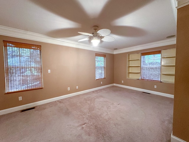 carpeted spare room featuring built in shelves, ceiling fan, and ornamental molding