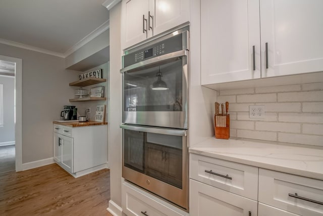 kitchen featuring double oven, white cabinetry, backsplash, ornamental molding, and light stone countertops