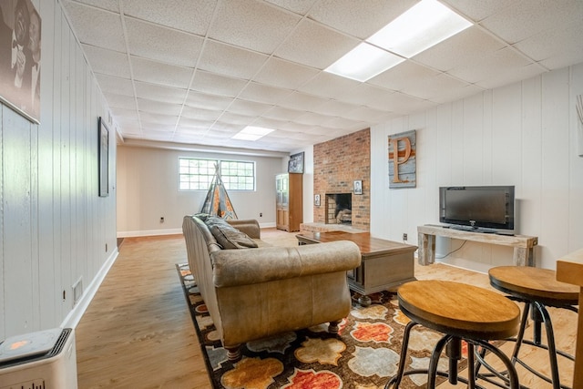 living room with a brick fireplace, a paneled ceiling, and light wood-type flooring