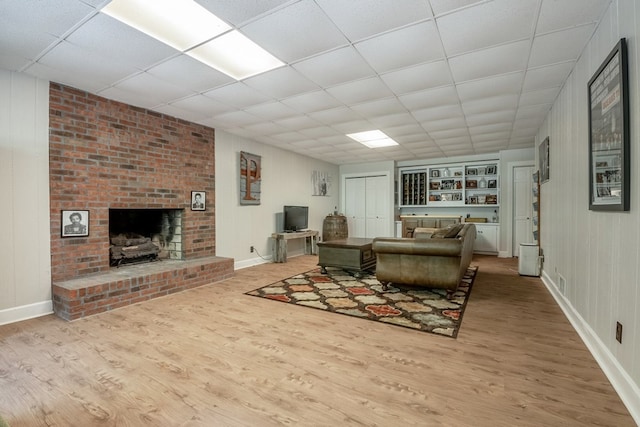 living room with a drop ceiling, a brick fireplace, hardwood / wood-style flooring, and built in shelves