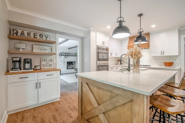 kitchen featuring a kitchen bar, light stone counters, light hardwood / wood-style flooring, pendant lighting, and white cabinets