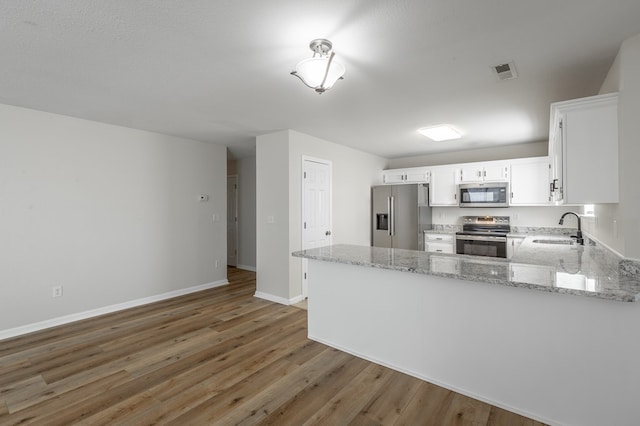 kitchen featuring sink, white cabinetry, stainless steel appliances, light stone countertops, and kitchen peninsula