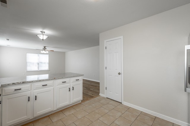 kitchen featuring white cabinetry, light tile patterned floors, ceiling fan, and light stone counters