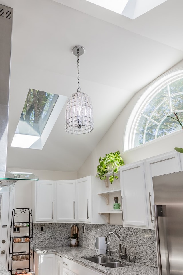 kitchen with sink, white cabinetry, stainless steel refrigerator, vaulted ceiling with skylight, and backsplash