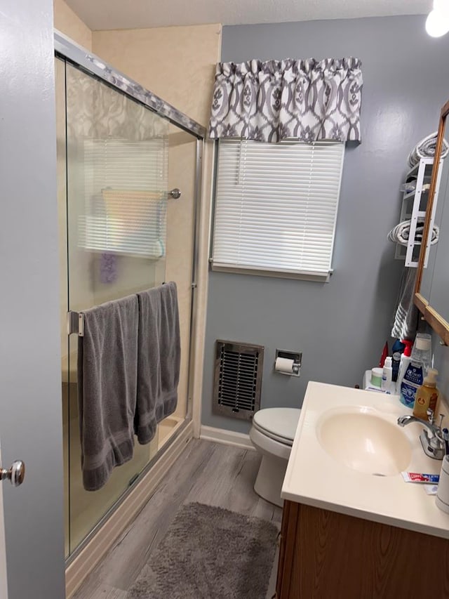 full bathroom featuring vanity, visible vents, wood finished floors, toilet, and a shower stall