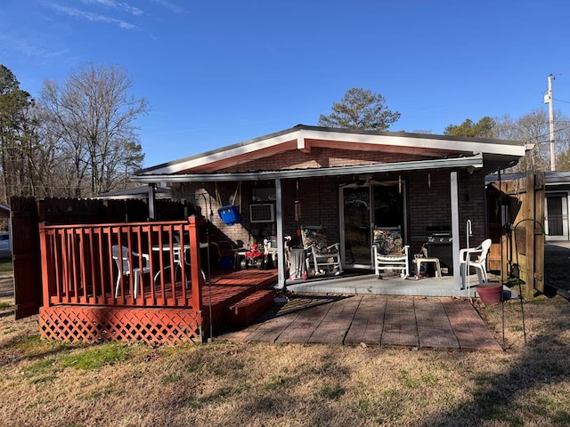 rear view of property featuring a wooden deck, a lawn, a patio, and brick siding