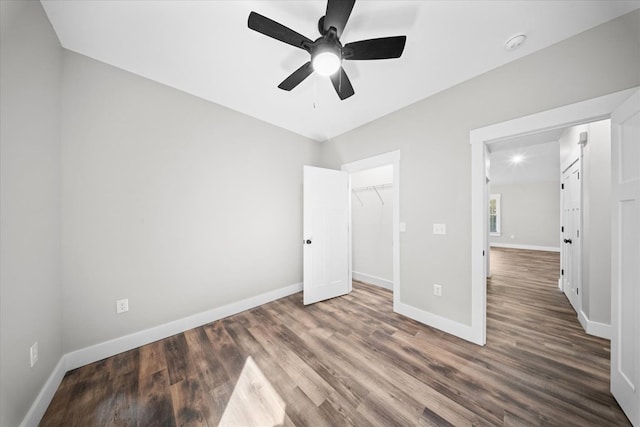 unfurnished bedroom with dark wood-type flooring, a walk in closet, ceiling fan, and a closet