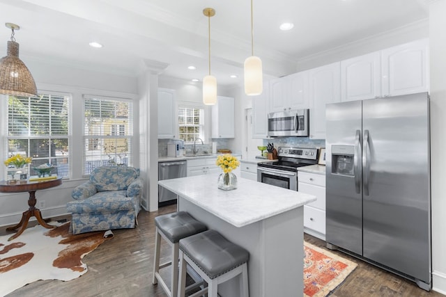 kitchen with appliances with stainless steel finishes, white cabinetry, hanging light fixtures, tasteful backsplash, and a kitchen island