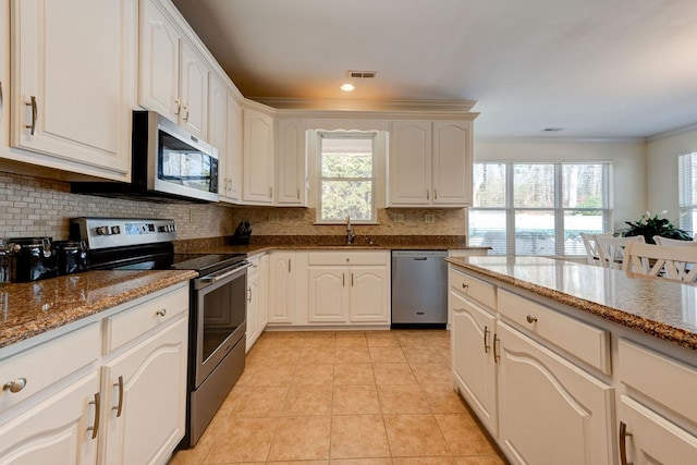 kitchen featuring appliances with stainless steel finishes, stone countertops, white cabinets, decorative backsplash, and crown molding