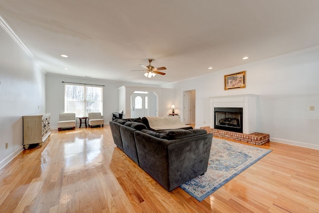 living room featuring crown molding, ceiling fan, a fireplace, and light wood-type flooring