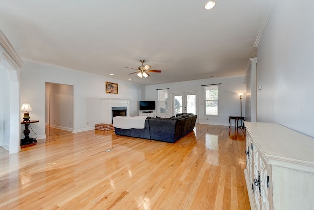 living room featuring french doors, a brick fireplace, light wood-type flooring, ornamental molding, and ceiling fan