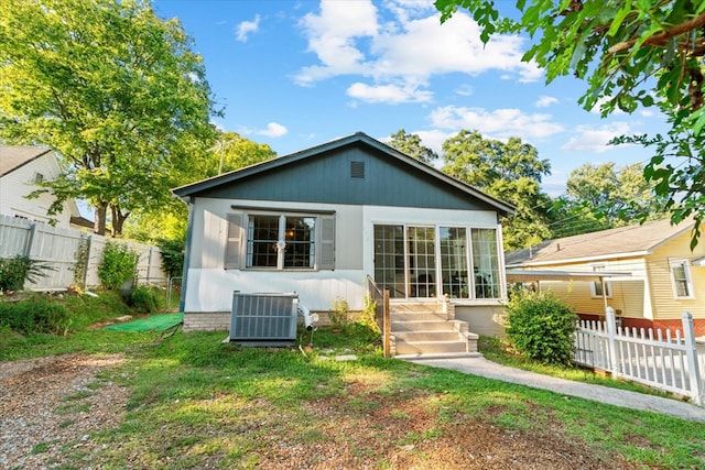 rear view of property featuring central AC unit and a lawn