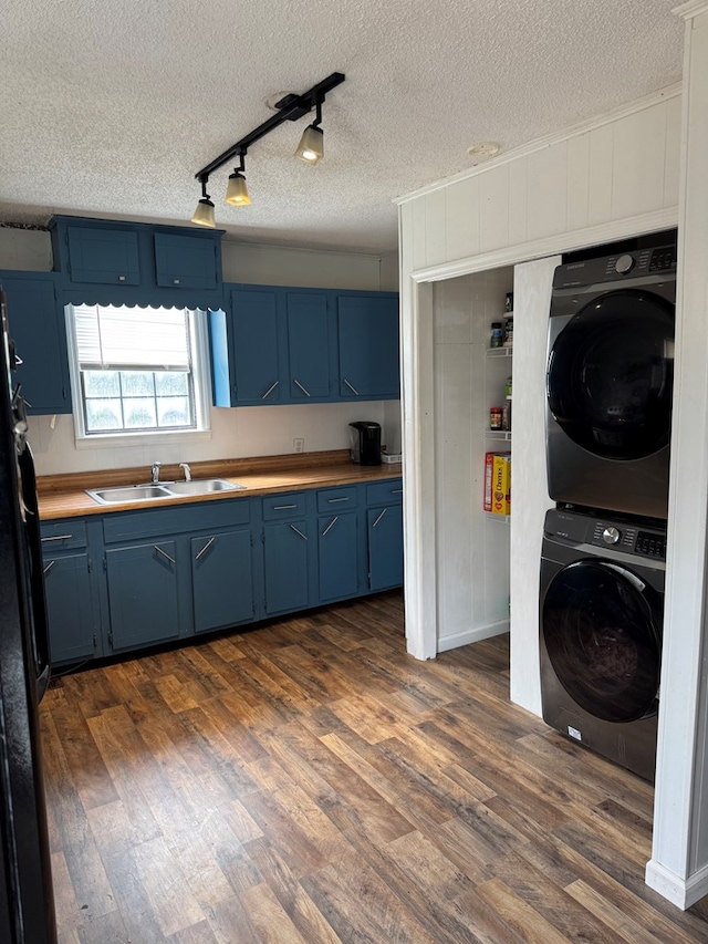 kitchen with dark wood finished floors, a sink, stacked washing maching and dryer, and blue cabinetry