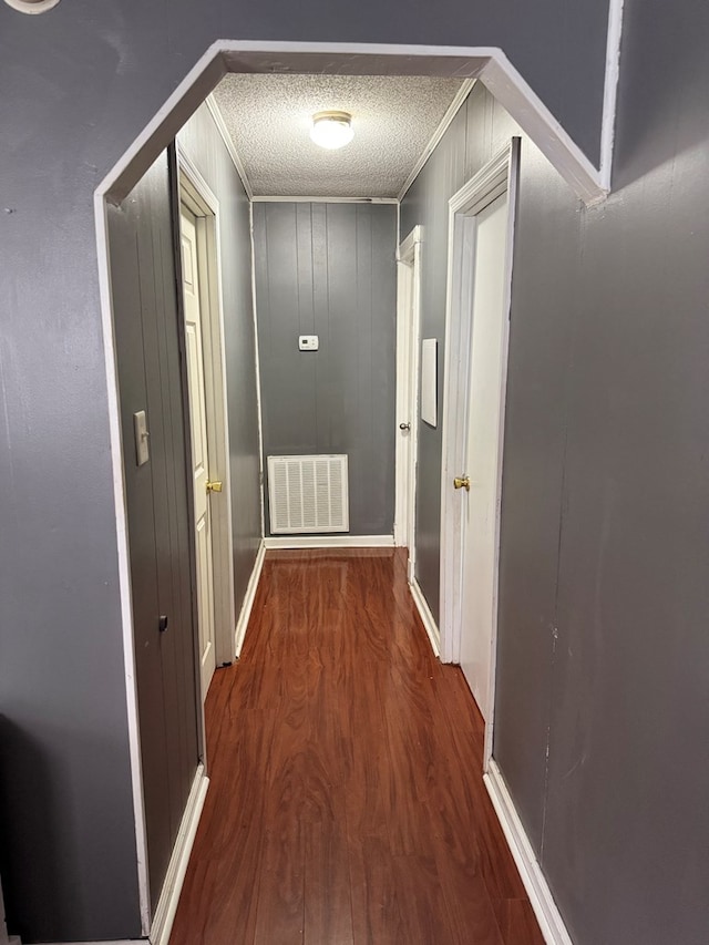 hall featuring a textured ceiling, ornamental molding, wood finished floors, and visible vents