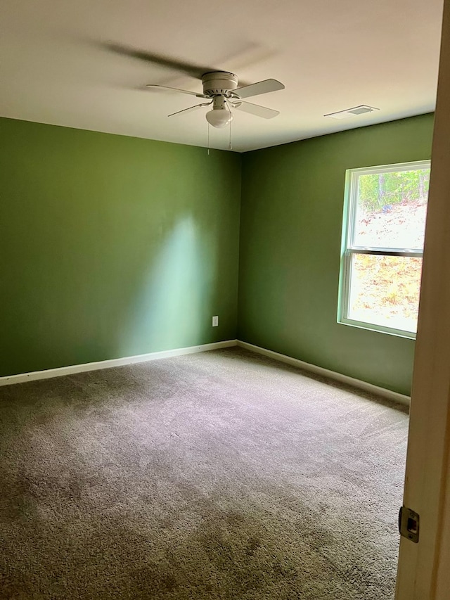 carpeted empty room with baseboards, a ceiling fan, and visible vents