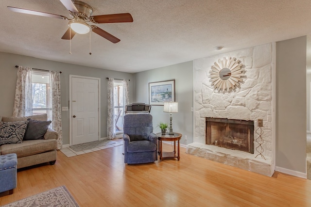 living room featuring hardwood / wood-style floors, a fireplace, a textured ceiling, and ceiling fan