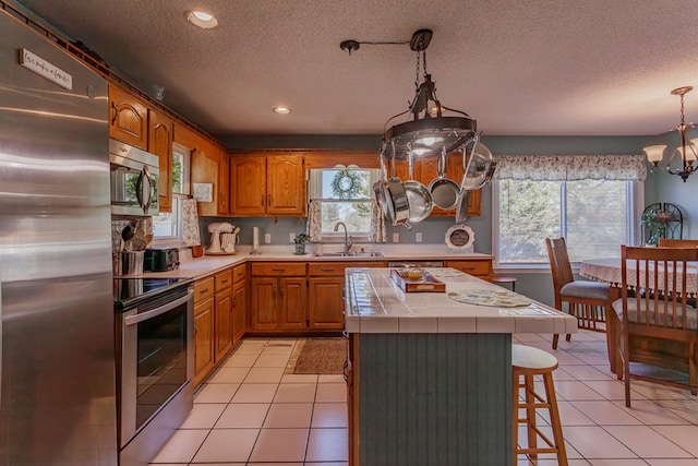 kitchen with sink, light tile patterned floors, tile counters, and stainless steel appliances