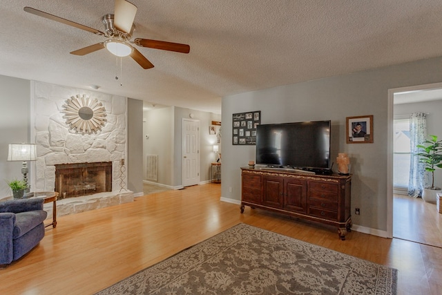 living room with hardwood / wood-style flooring, ceiling fan, a fireplace, and a textured ceiling