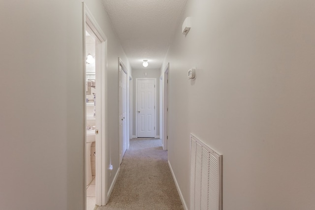 corridor with light colored carpet and a textured ceiling