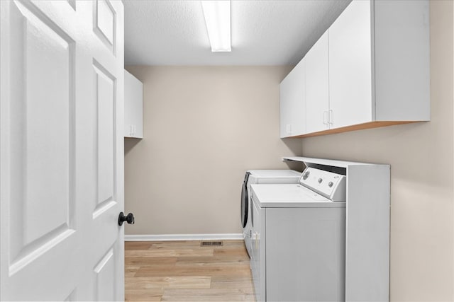 laundry room with cabinets, washing machine and clothes dryer, a textured ceiling, and light wood-type flooring