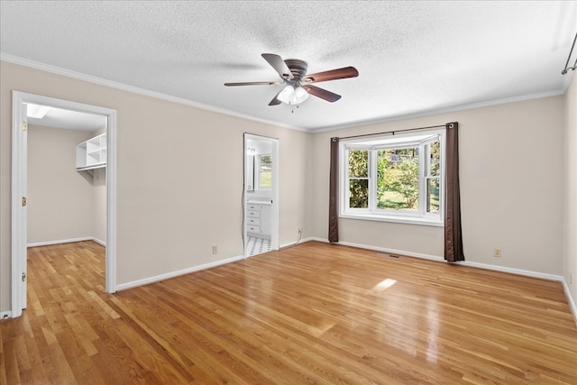 unfurnished bedroom with crown molding, a walk in closet, light hardwood / wood-style floors, and a textured ceiling