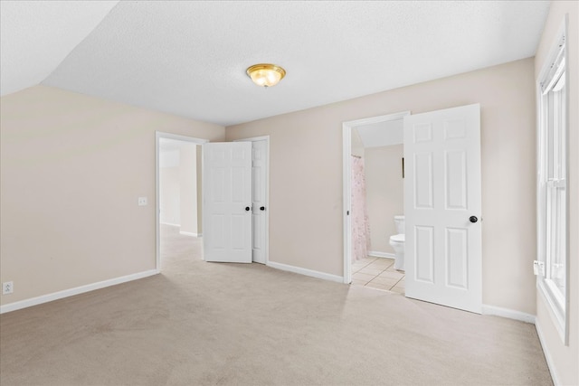 unfurnished bedroom with light carpet, connected bathroom, and a textured ceiling