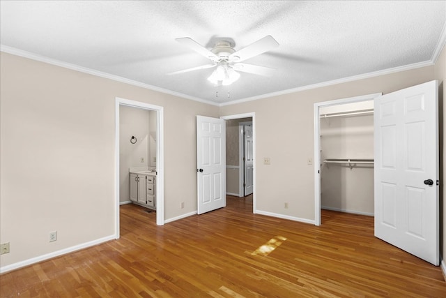 unfurnished bedroom with crown molding, a walk in closet, wood-type flooring, a textured ceiling, and a closet