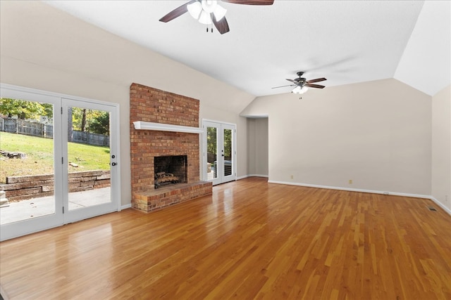 unfurnished living room featuring a healthy amount of sunlight, lofted ceiling, hardwood / wood-style floors, and a brick fireplace