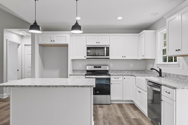 kitchen with appliances with stainless steel finishes, white cabinetry, hanging light fixtures, light hardwood / wood-style floors, and a kitchen island