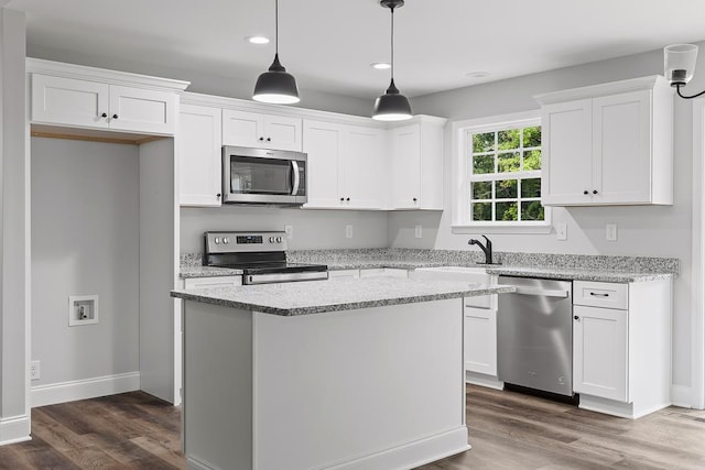 kitchen with white cabinetry, decorative light fixtures, a kitchen island, stainless steel appliances, and light stone countertops