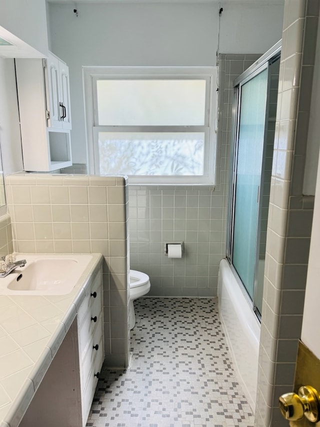 full bathroom with vanity, combined bath / shower with glass door, tile walls, and toilet